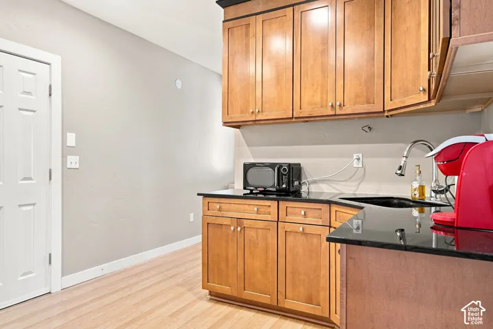 Warm-toned wood cabinetry with upper and lower storage, black countertops, and a stainless steel sink with a gooseneck faucet