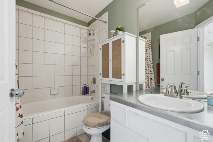 Bright bathroom featuring white subway tile surround, dual vanity with gray countertop and brushed nickel faucet, oval vessel sink, white cabinetry with wood-finish accents, and a separate soaking tub with tile enclosure and glass shower door