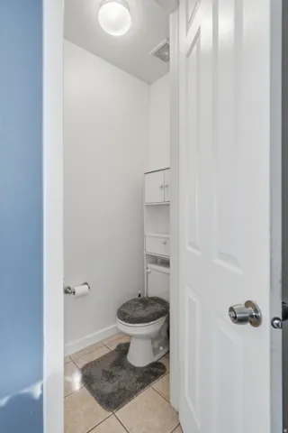 Recessed lighting fixture, white paneled door, built-in white shelving unit, tile flooring, and white toilet