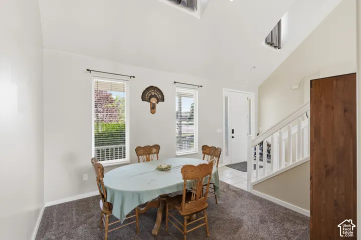 Vaulted ceiling, two windows with blinds, white trim, white door, staircase with white railing