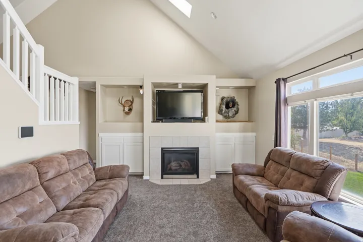 Vaulted ceiling, built-in shelving, fireplace with tile surround, large windows, and white staircase railing