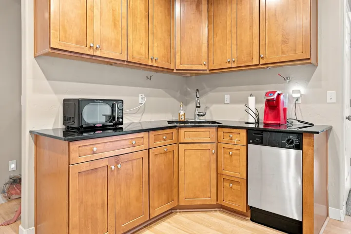 Wood-finish cabinetry with silver-tone hardware, black countertops, stainless steel dishwasher, and a stainless steel sink with a chrome faucet