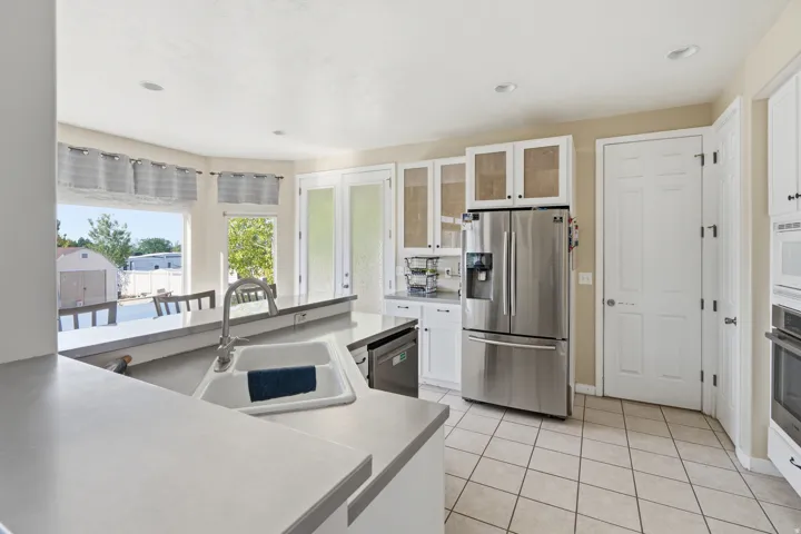 Kitchen with white cabinetry, stainless steel appliances, a double basin sink, light-toned countertops, and tiled flooring