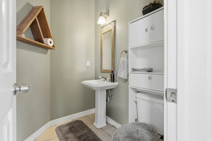 Pedestal sink, ceramic tile flooring, built-in storage cabinetry, wall-mounted mirror, and overhead vanity lighting