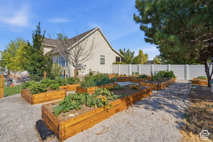 Backyard featuring multiple raised garden beds, gravel pathways, a white privacy fence, and mature trees