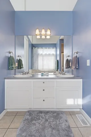 Dual vanity with undermount sinks, white cabinetry, and a full-width mirror