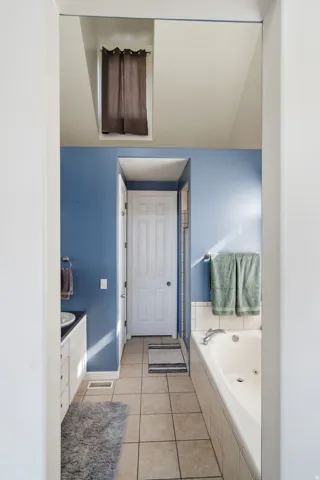 Recessed bathtub with tiled surround, single vanity with integrated sink, panel cabinetry, and tiled flooring