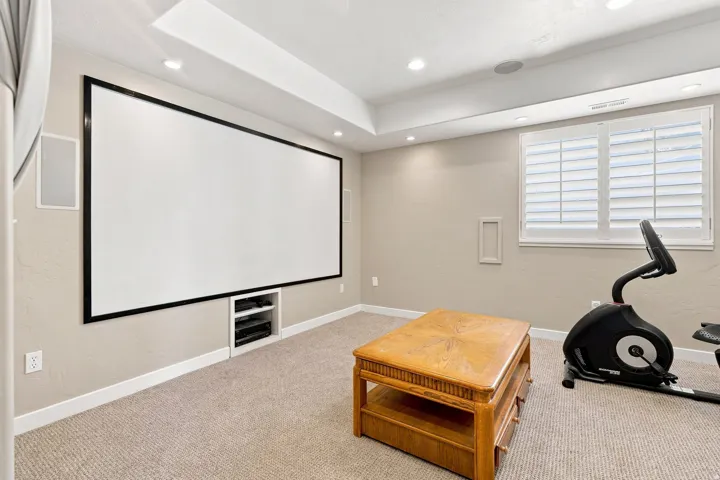 Built-in projection screen with recessed media storage, integrated ceiling speakers, recessed lighting, and plantation shutters