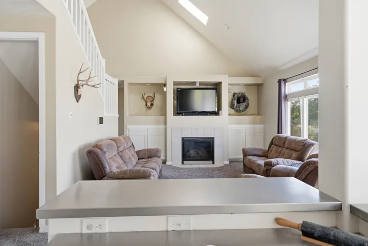 Vaulted ceiling with skylight, fireplace with tile surround, built-in shelving, white cabinetry, and large windows