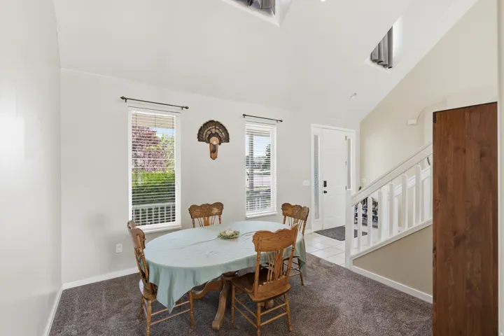 Vaulted ceiling, two windows with blinds, white trim, white door, staircase with white railing