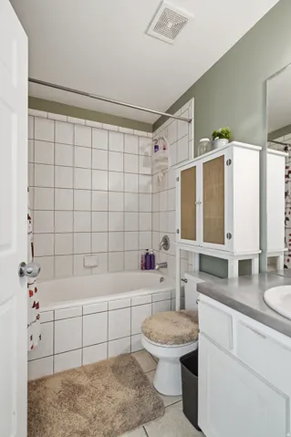 Bathtub with white tile surround, white vanity with integrated sink, and wall-mounted mirror