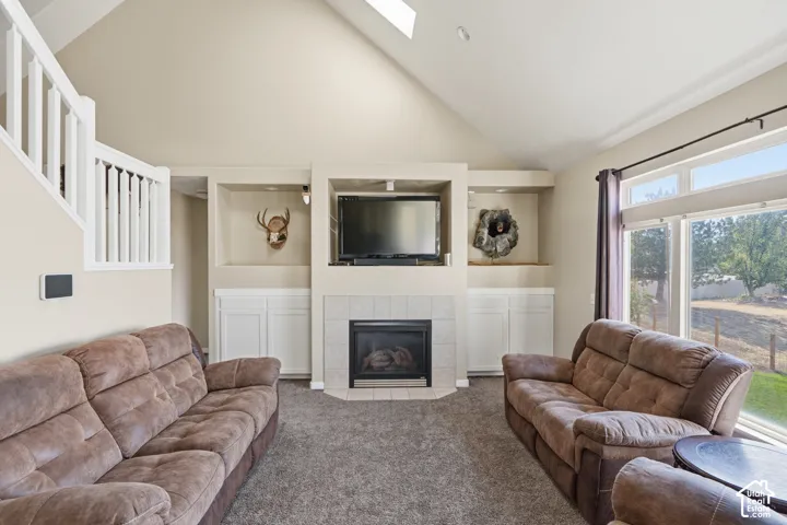 Vaulted ceiling, built-in shelving, fireplace with tile surround, large windows, and white staircase railing