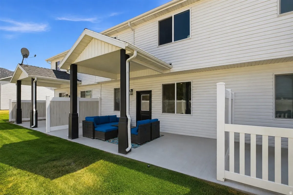 Covered patio with dark support columns, white vinyl siding, and a manicured lawn