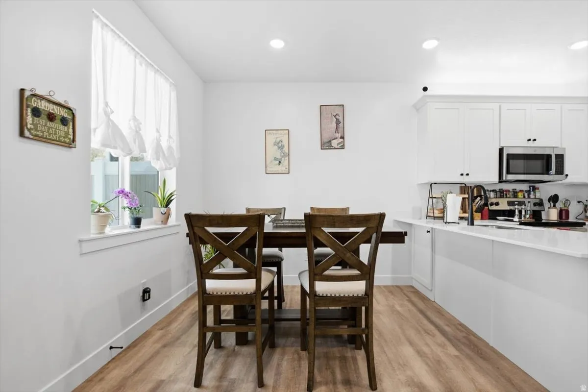 White cabinetry with matte black hardware, stainless steel microwave, wood-finish flooring, recessed lighting, and a kitchen island with a sink