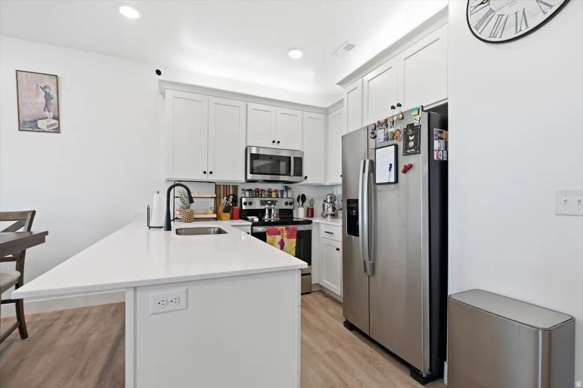 Kitchen featuring white cabinetry, stainless steel appliances, a white island with an undermount sink, a matte black faucet, and wood-finish flooring