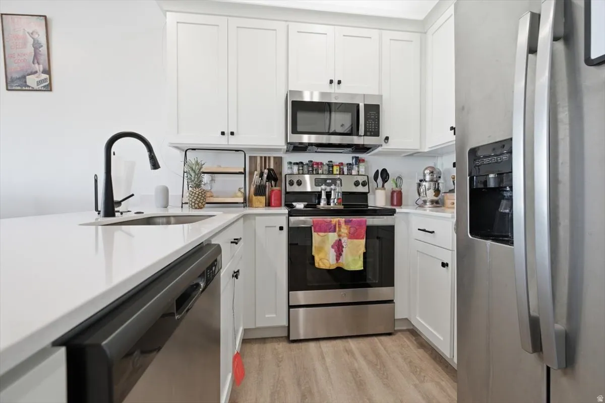 White shaker cabinetry, stainless steel appliances, matte black faucet, and wood-finish flooring