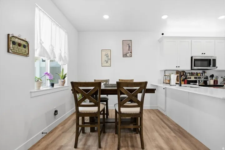 White cabinetry with matte black hardware, stainless steel microwave, wood-finish flooring, recessed lighting, and a kitchen island with a sink