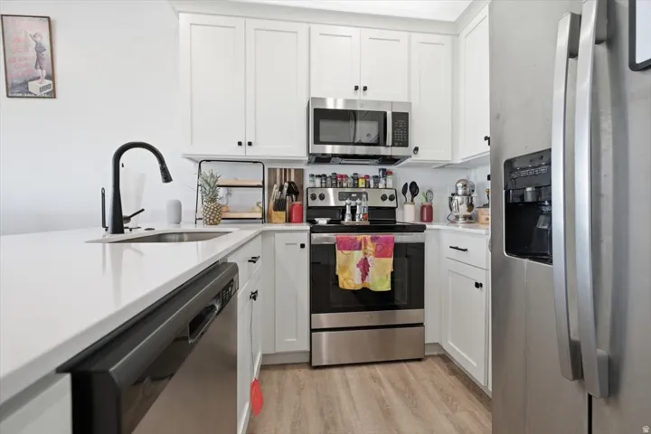 White shaker cabinetry, stainless steel appliances, matte black faucet, and wood-finish flooring