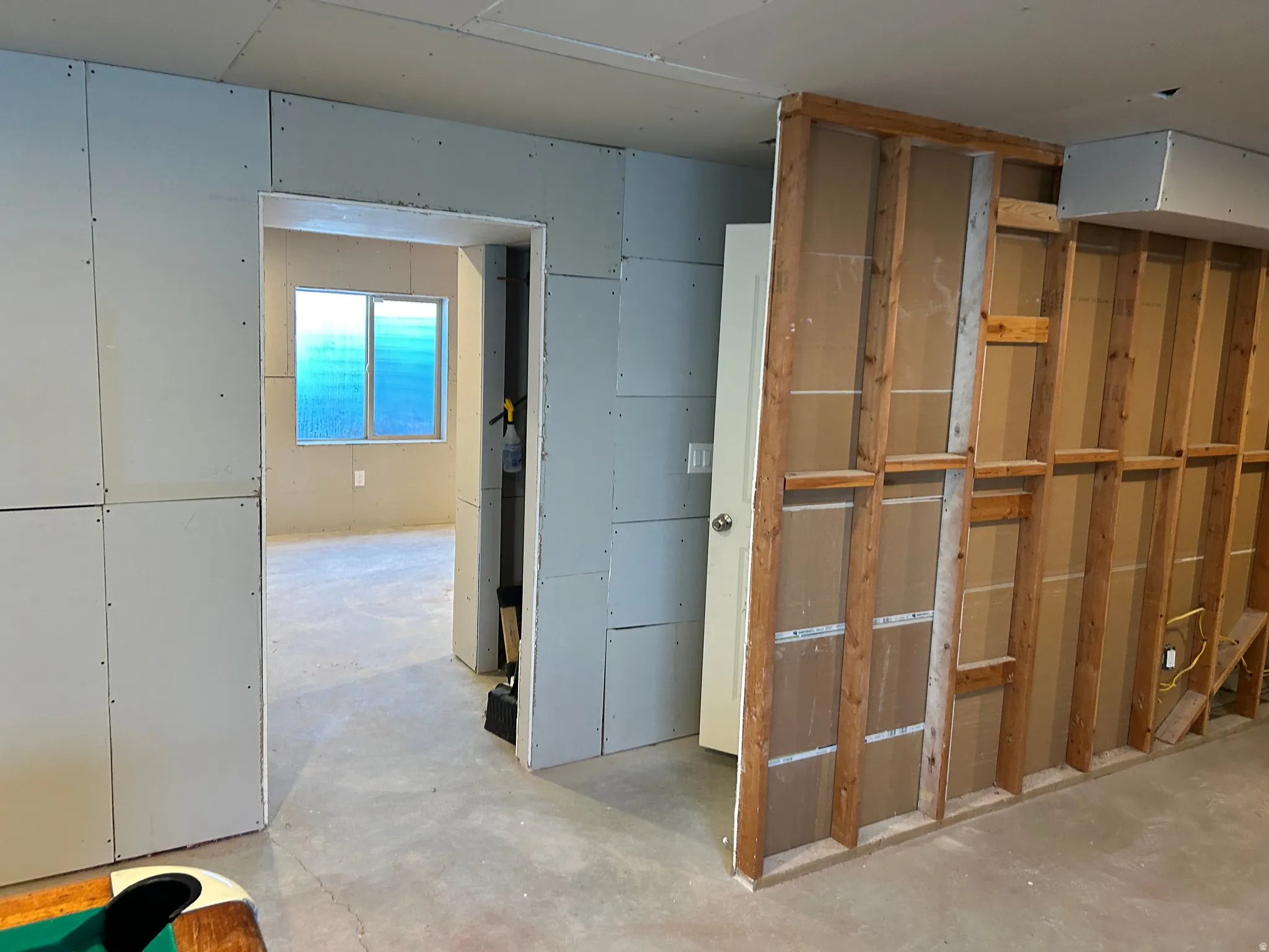 Unfinished interior space with exposed framing and a drywall-paneled wall, featuring an interior doorway and a window