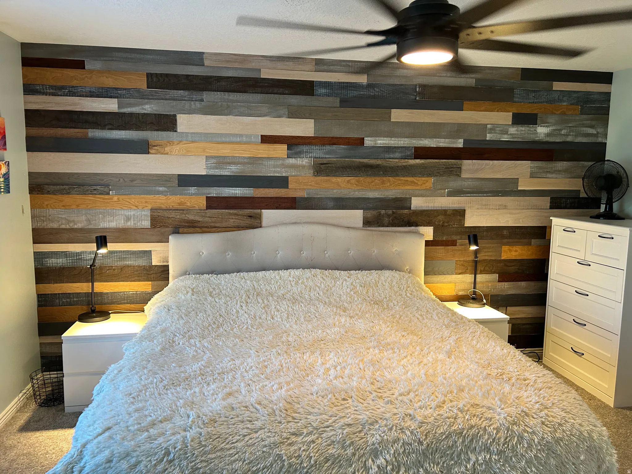 Accent wall with horizontal wood planks in varied tones, tufted headboard, and ceiling fan with integrated lighting