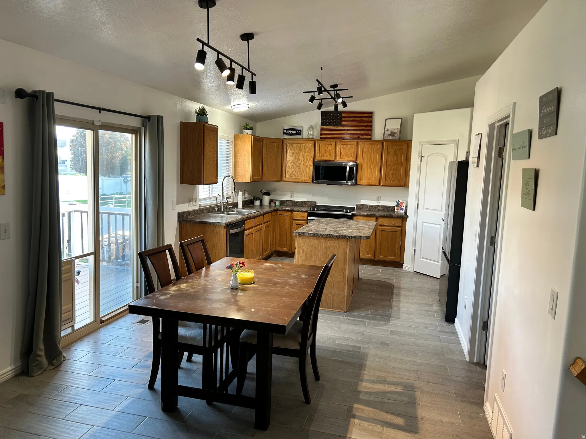 Open-concept kitchen and dining area featuring wood-finish cabinetry, stainless steel appliances, wood-finish flooring, and dual pendant lighting fixtures