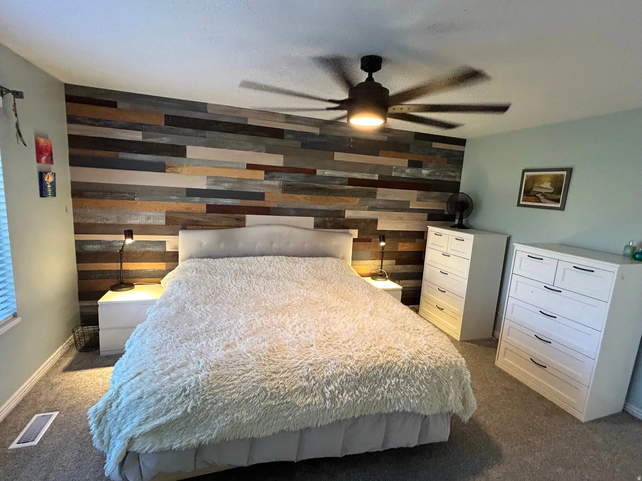 Accent wall featuring varied wood-finish planks, ceiling fan with integrated lighting, and neutral carpeting