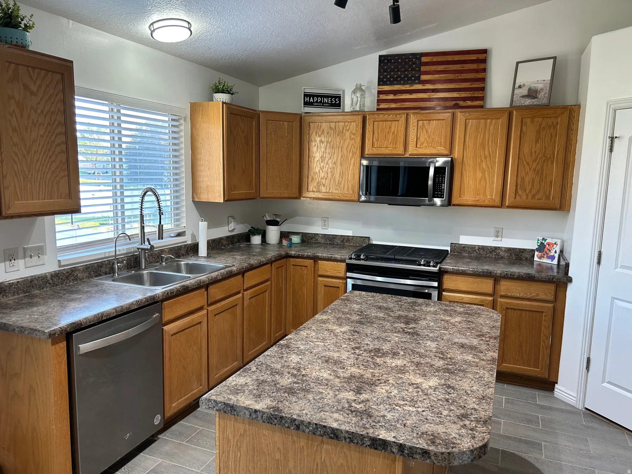 Kitchen featuring wood cabinetry, stainless steel appliances, a center island with countertop, and grey tile flooring