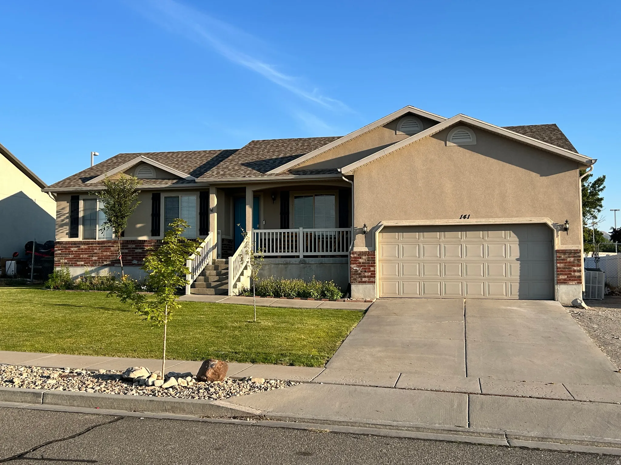 Stucco and brick exterior with a two-car garage, concrete driveway, and a covered porch with white railing