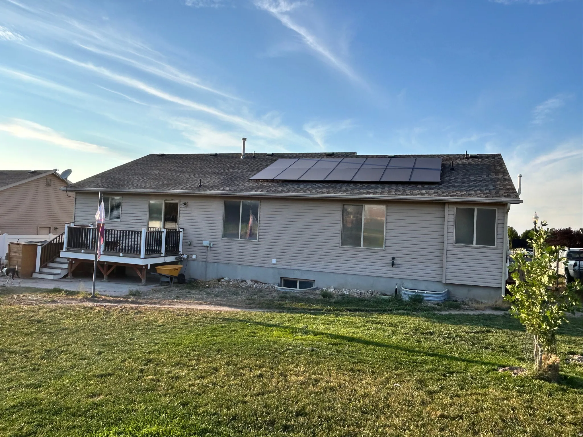 Rear exterior featuring a spacious deck with railing, solar panels, and a level yard