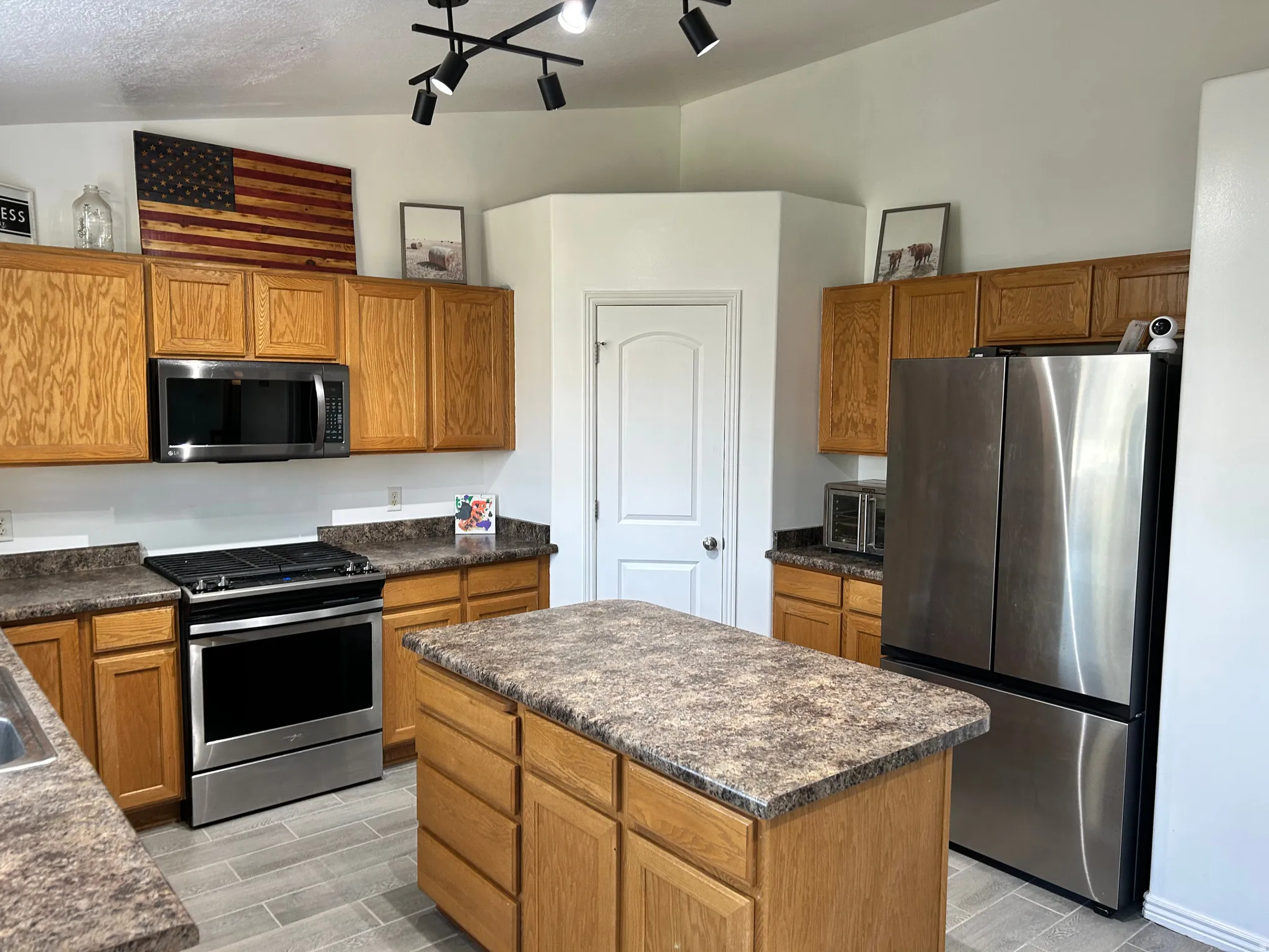 Kitchen featuring wood-finish cabinetry, stainless steel appliances, a central island with a countertop, and track lighting