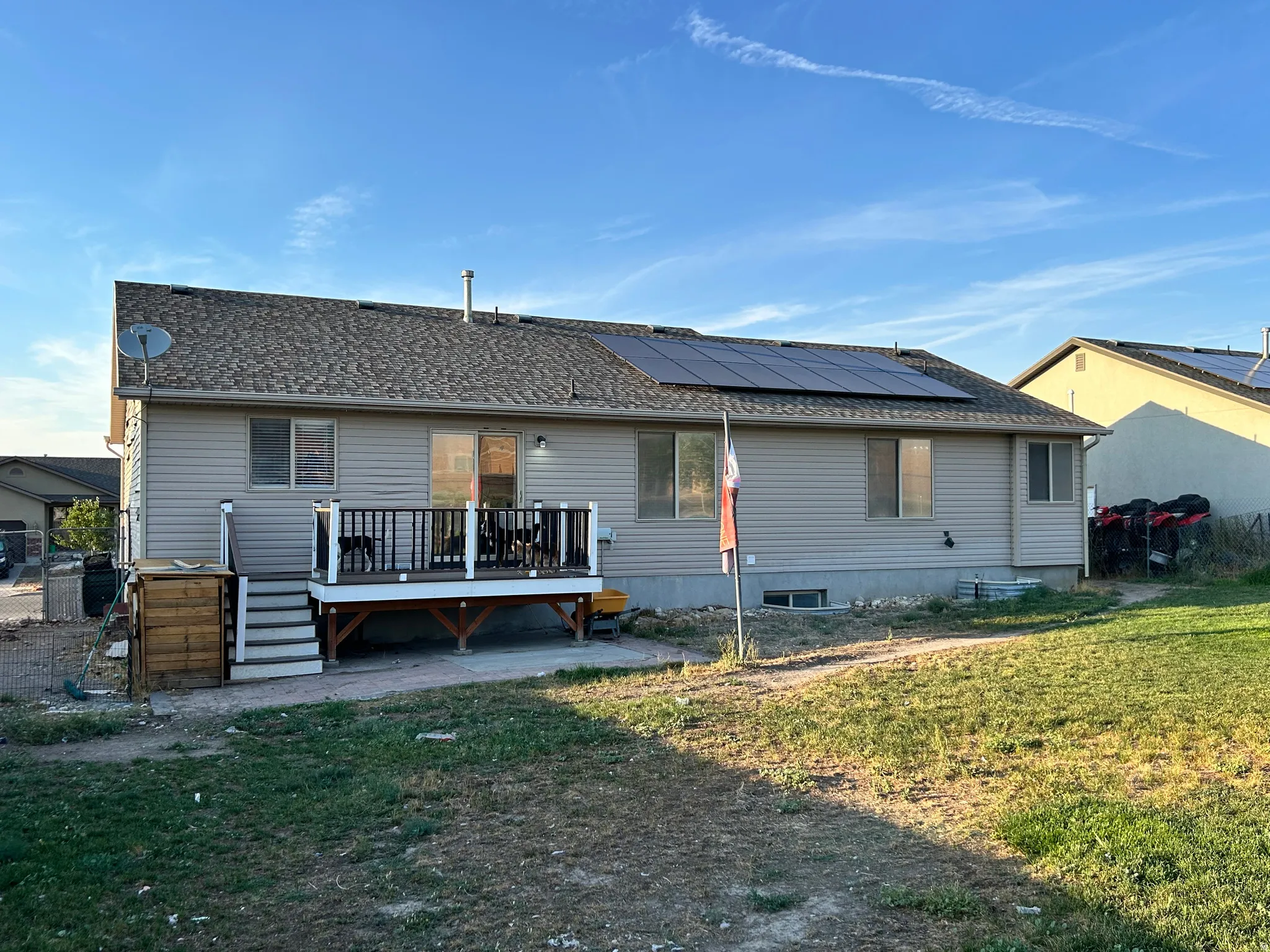 Rear exterior featuring a composite deck with white and black railings, shingle roof, solar panels, and beige siding