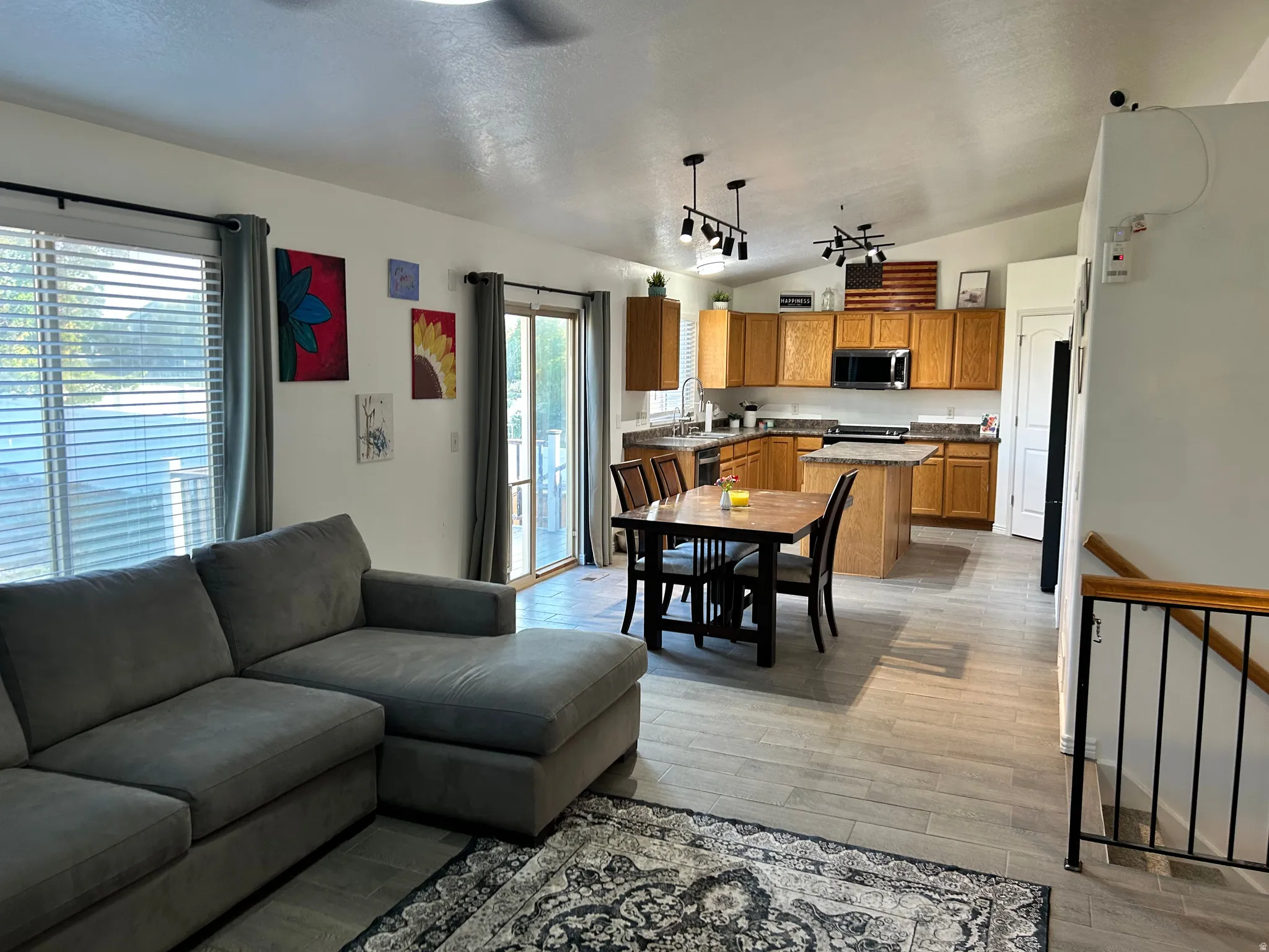 Vaulted ceilings with track lighting fixtures, wood-finish flooring, and built-in wood cabinetry with a kitchen island