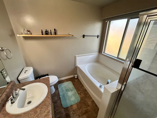 Built-in soaking tub, vanity with integrated sink, chrome faucet, window, and wood-finish flooring