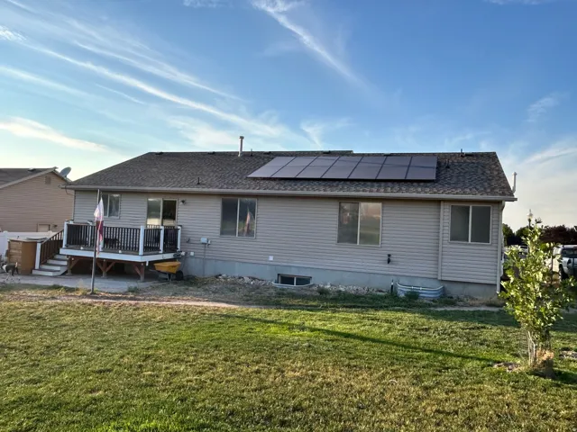 Rear exterior featuring a spacious deck with railing, solar panels, and a level yard