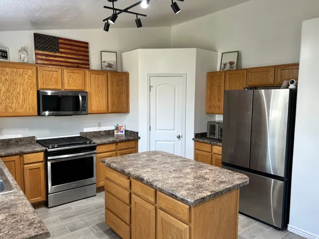 Kitchen featuring wood-finish cabinetry, stainless steel appliances, a central island with a countertop, and track lighting