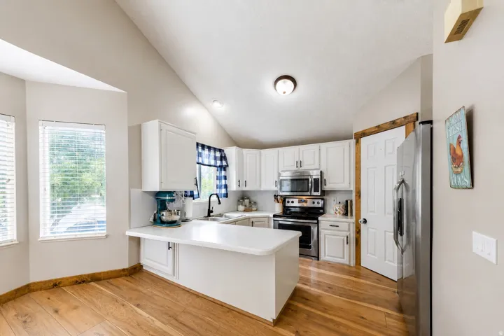 White cabinetry with stainless steel appliances, solid surface countertops, a vaulted ceiling, and wood-finish flooring