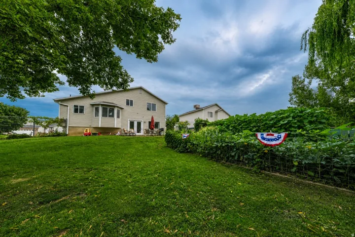 Expansive green lawn, bay window, rear patio access, and garden area with established plantings