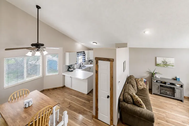 Open-concept living area featuring hardwood flooring throughout, a ceiling fan with integrated lighting, and a well-appointed kitchenette with white cabinetry and a sink
