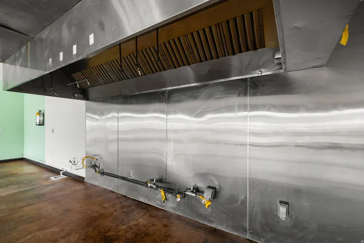 Stainless steel commercial-grade hood system, stainless steel wall paneling, exposed utility lines, and concrete flooring