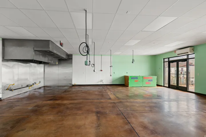 Commercial-grade exhaust hood, stainless steel wall paneling, exposed gas lines, dark concrete flooring, and drop ceiling with integrated lighting