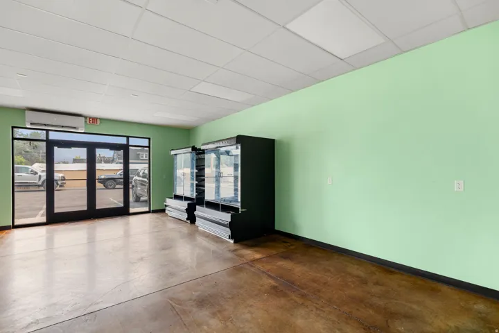 Full glass paneled entry doors, concrete flooring, drop ceiling, and wall-mounted climate control unit