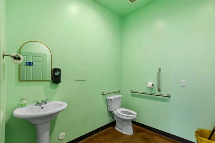 Pedestal sink with chrome-finish faucet, toilet with grab bars, and polished concrete flooring
