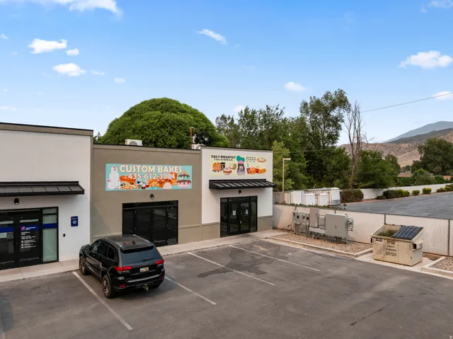 Commercial building featuring multiple storefronts with awnings, a paved parking area, and a mountainous backdrop