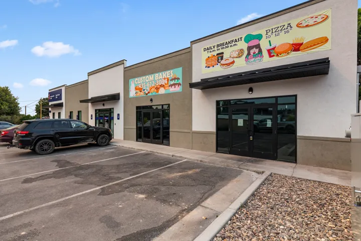 Commercial storefronts featuring large glass entry doors, dark awnings, and a paved parking area