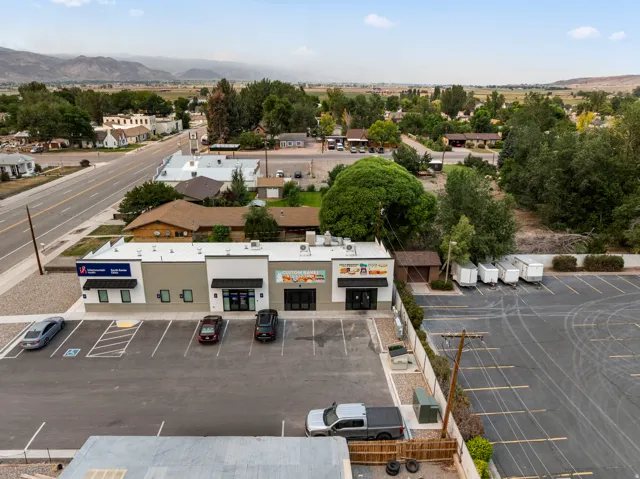 Commercial building with multiple storefronts, an expansive paved parking lot, and a metal roof
