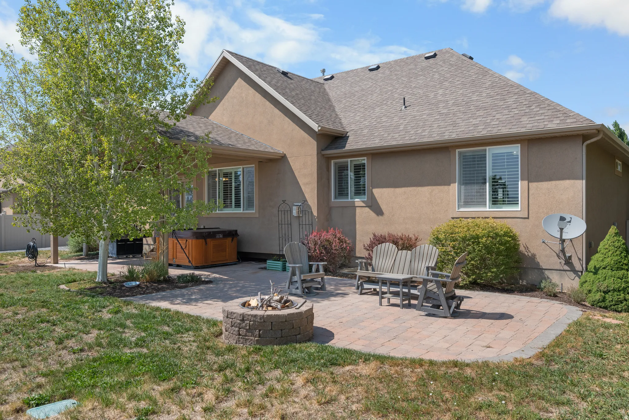 Expansive paver patio featuring a built-in stone fire pit and a wood-finish hot tub