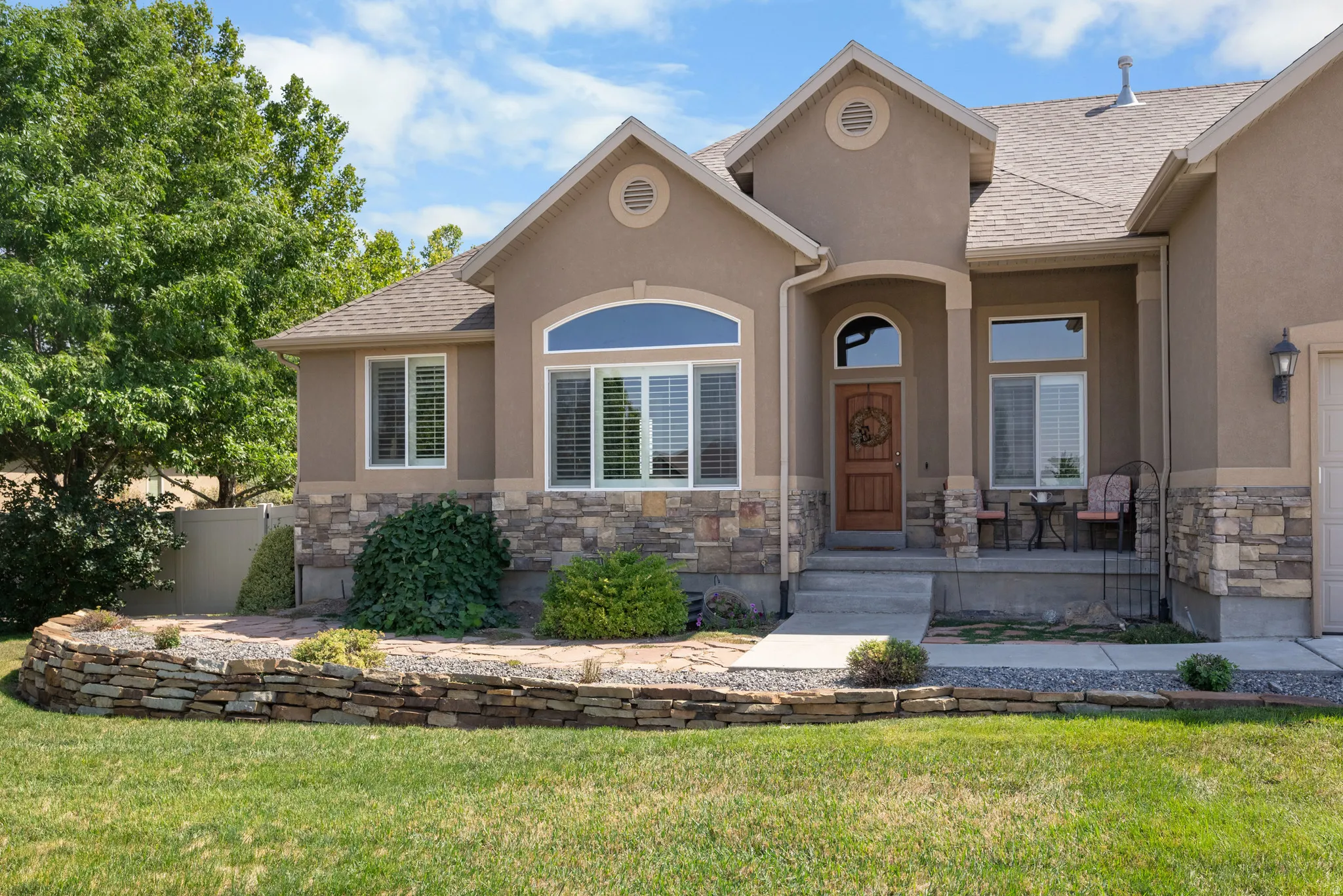 Stucco exterior with stone accent, arched entry, gabled roof, and stone retaining wall