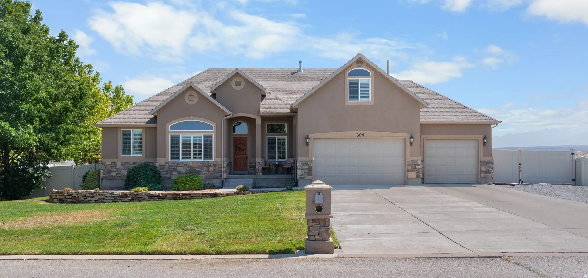 Stucco exterior with stone accents, a three-car garage, mature landscaping, and a concrete driveway