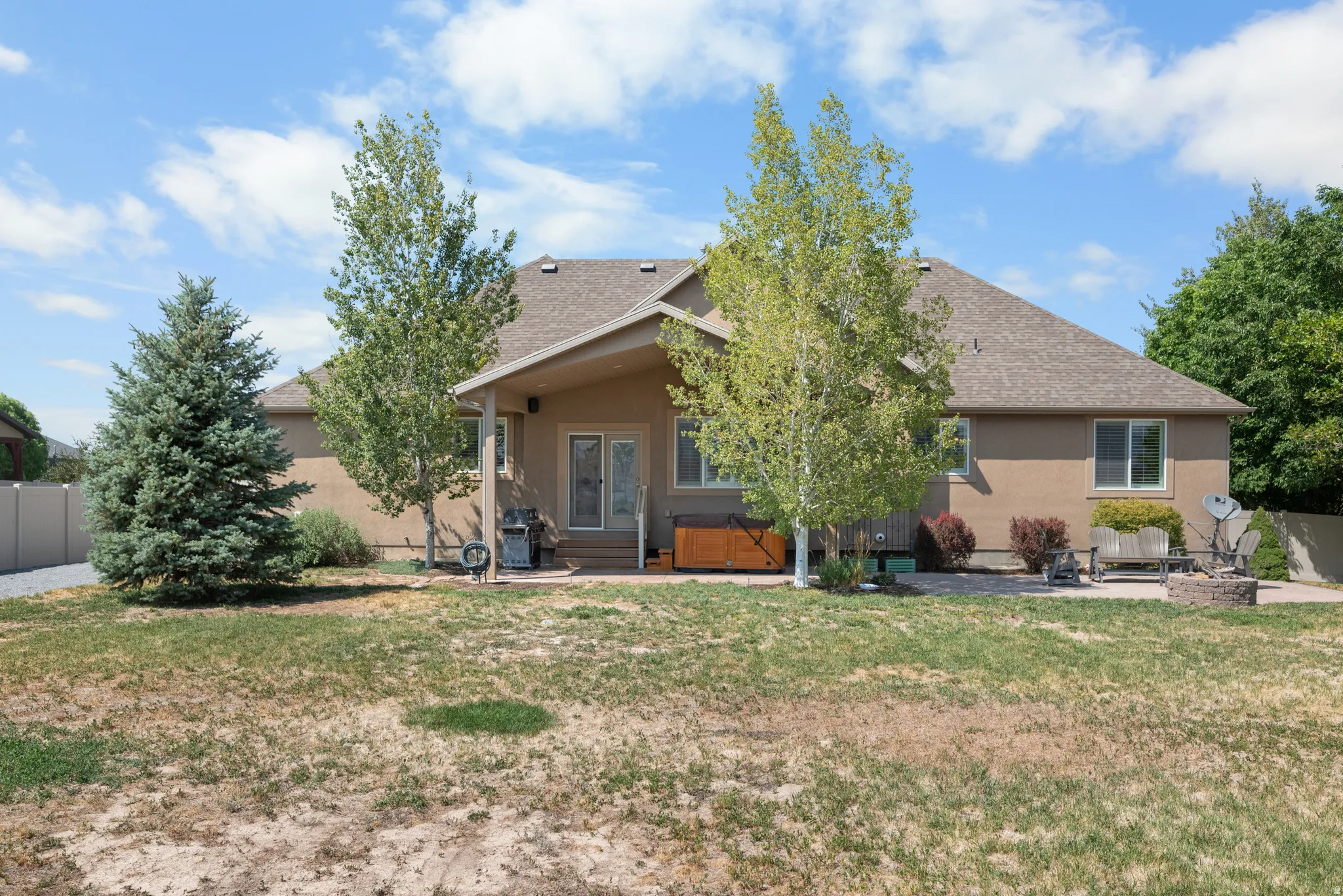 Rear exterior featuring a covered patio, multiple windows, and a paved outdoor area with a fire pit