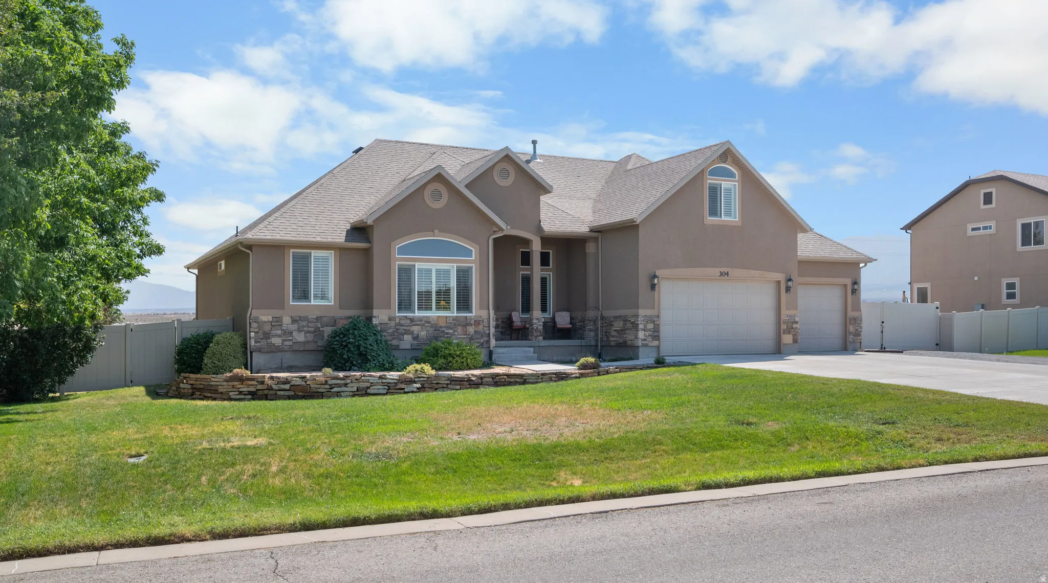 Stucco exterior with stone accent, arched window details, two-car garage, established front landscaping, and concrete driveway